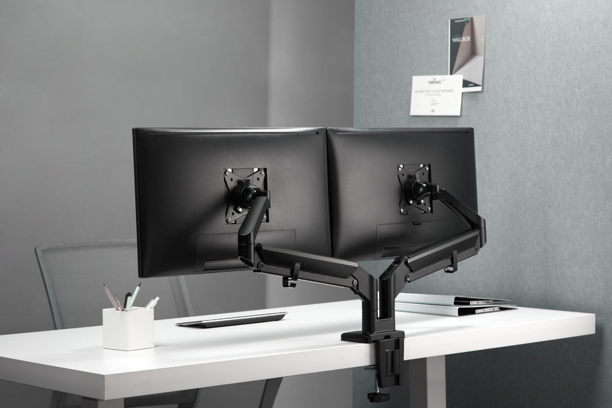 Office desk with two monitors on a dual monitor arm beside a window