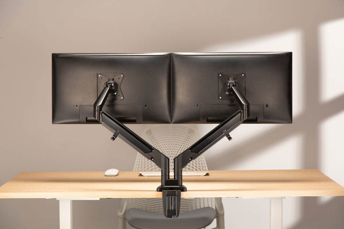 Two monitors on a dual monitor arm on a wooden desk in warm light