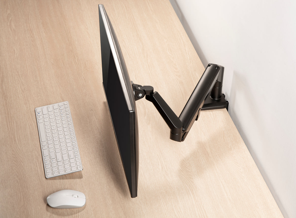 Wooden desk with a monitor on a black gas spring arm and a white keyboard