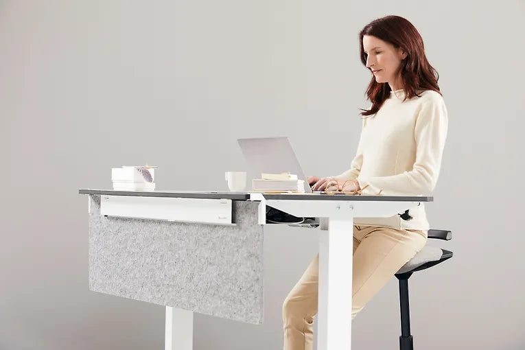 Woman working at a standing desk while perching on a blue Muvman stool