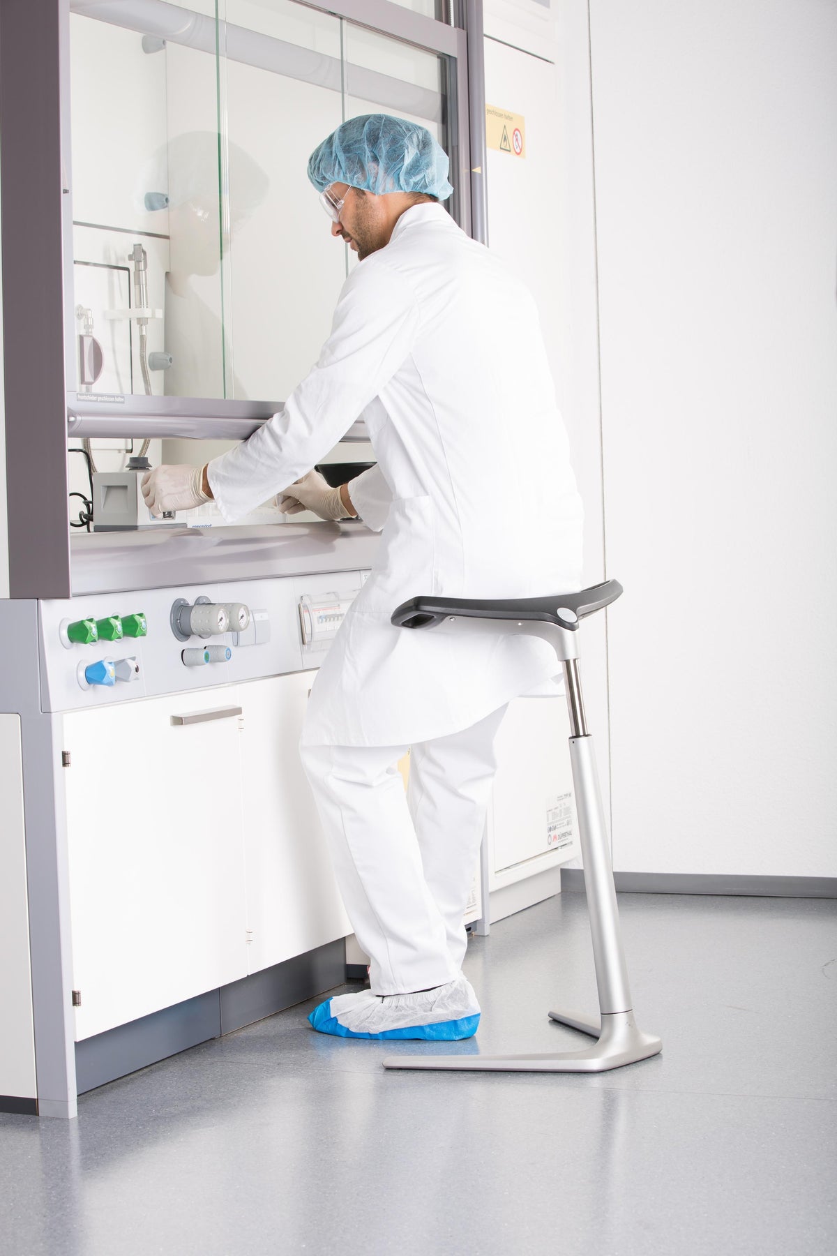 Laboratory technician in protective clothing using a FIN leaning chair at a bench
