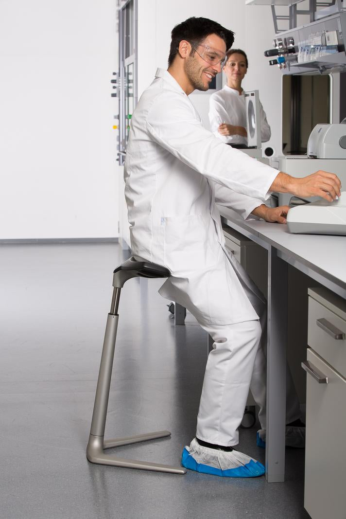 Worker in white overalls leaning on a FIN chair beside a laboratory bench