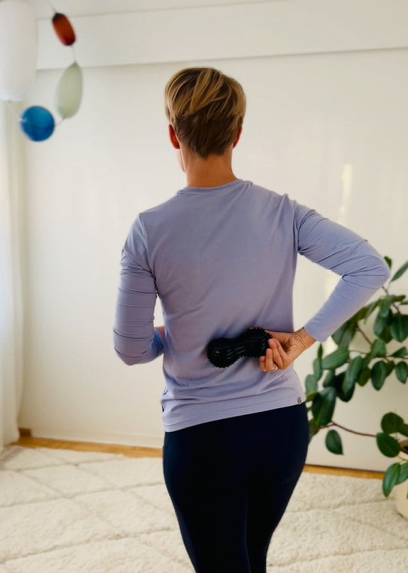 Woman seen from behind using a massage roller on her shoulder