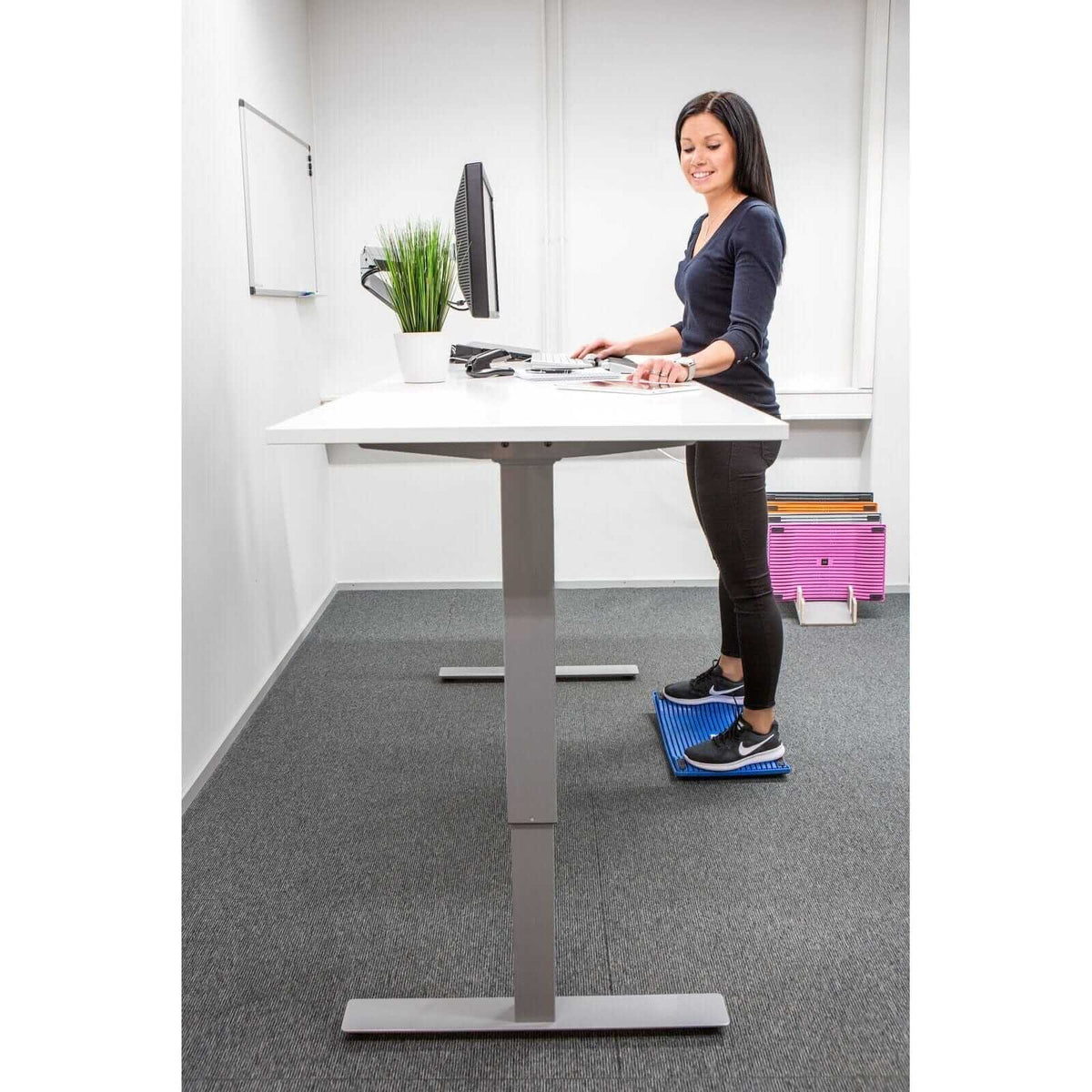 Woman using Gymba activation board in Tidepool Green at a standing desk, promoting active movement and improved workplace wellness.
