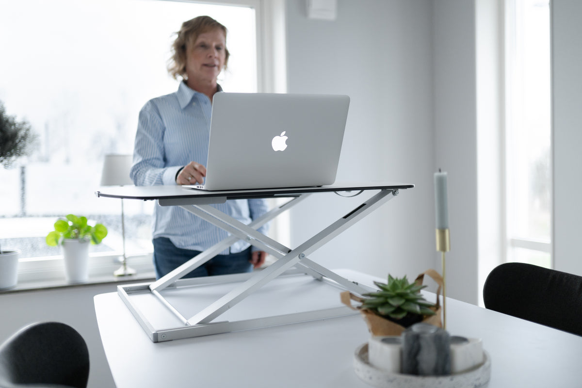 Man working at a standing desk converter on a table in a bright office