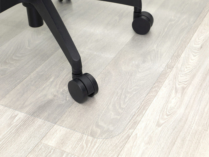 Close-up of a chair castor rolling on a transparent mat over a wooden floor
