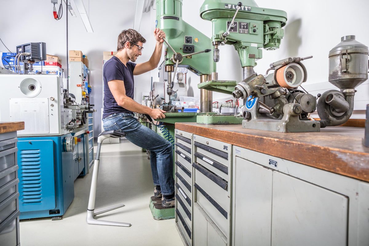 Worker in a machine shop leaning on a FIN leaning chair at a workbench
