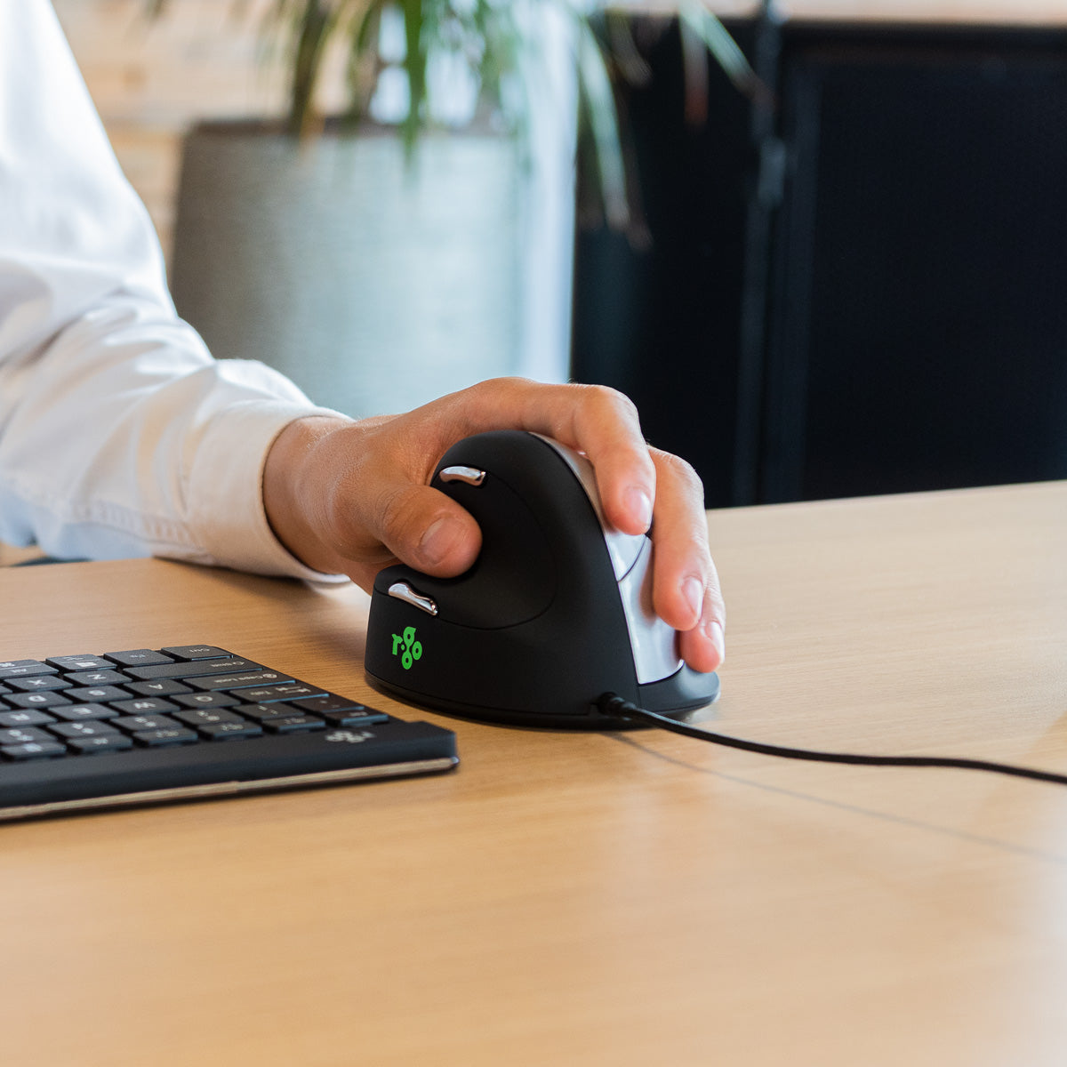 Hand using an HE Mouse left-handed vertical mouse at a desk with a keyboard