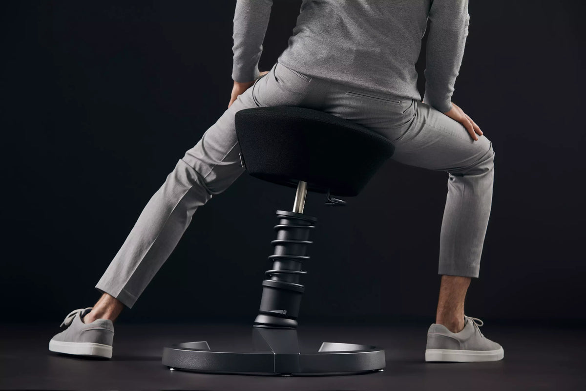 Person perching on a Swopper active chair against a dark background