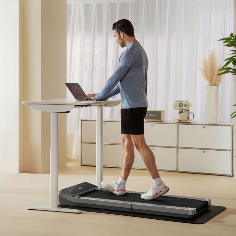 Man walking on a WalkingPad V2 treadmill while working at a standing desk with a laptop