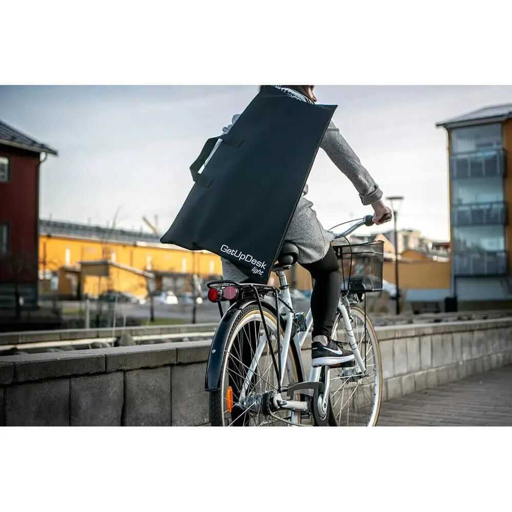 Person cycling with GetUpDesk light carry bag, easily transporting it through city streets.