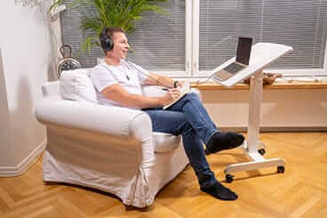 Man working on a laptop at a GetUpDesk Tilt desk while seated in an armchair