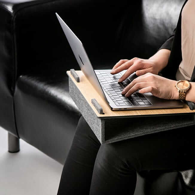 Woman typing on a laptop resting on a Lapsteri stand while seated in an armchair