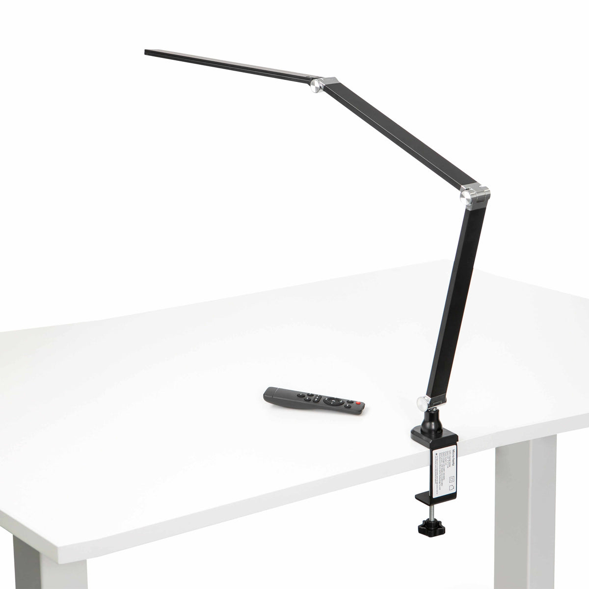 Black LED desk lamp with long metal arm and aluminium joints on white desk, featuring a remote control, ideal for modern workspaces.