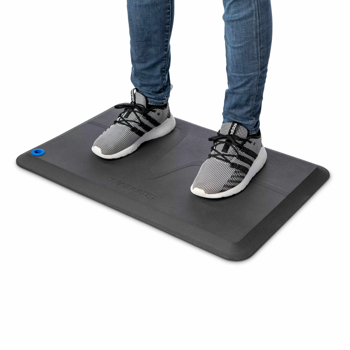Person in trainers standing on a black StandMat workstation mat