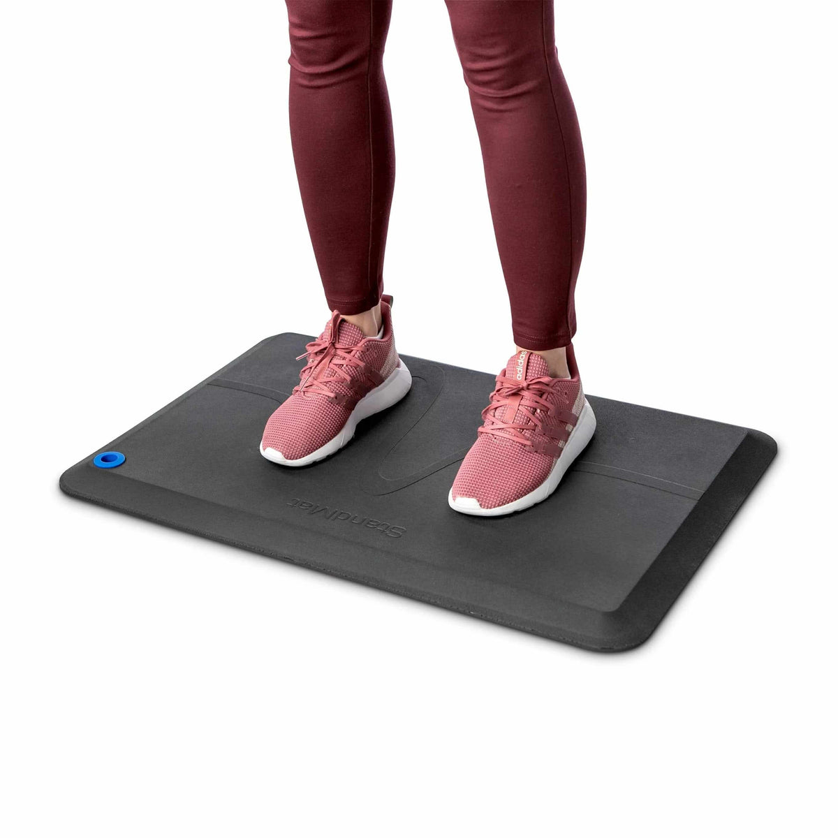 Person in trainers standing on a black StandMat workstation mat